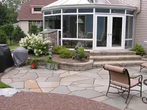 A patio with a grill and chairs in front of a house.