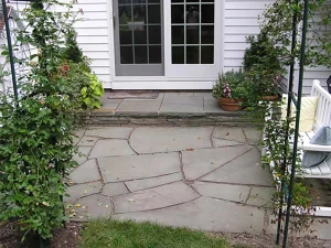 A stone patio with a white door and white fence.