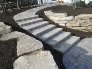 Outdoor stone pathway with steps and a curved retaining wall for landscape enhancement.