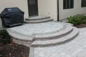 Semi-circular gray block steps leading up patio with barbeque.