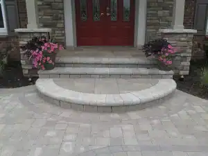 Grey stone block entryway steps and patio with potted flowers on each side.