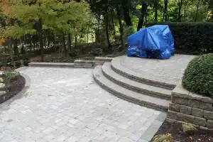 Semi-circular gray block steps leading up patio with barbeque.