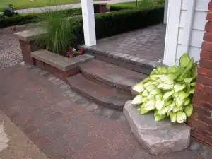 Red block steps with paved porch and plants.