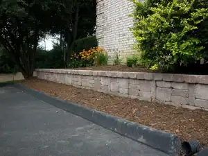 Low brick retaining wall bed with shrubs and flowers.