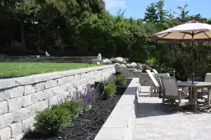 Retaining wall with paved patio and outdoor furniture with umbrella table.